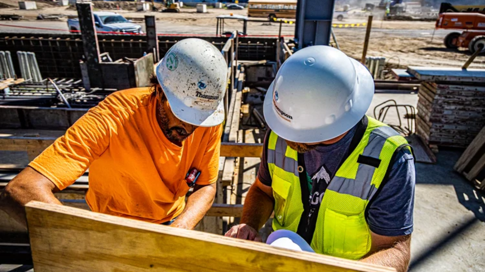 two construction workers looking at blue prints on a job site.